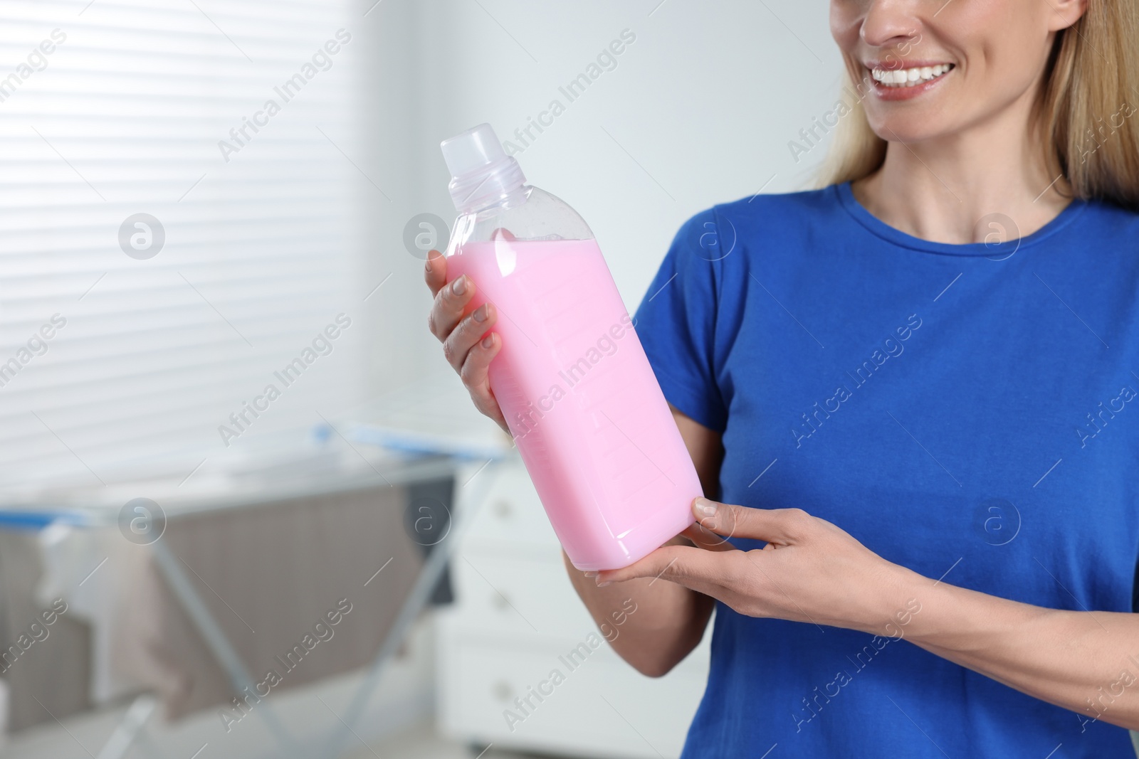 Photo of Woman holding fabric softener in bathroom, closeup. Space for text