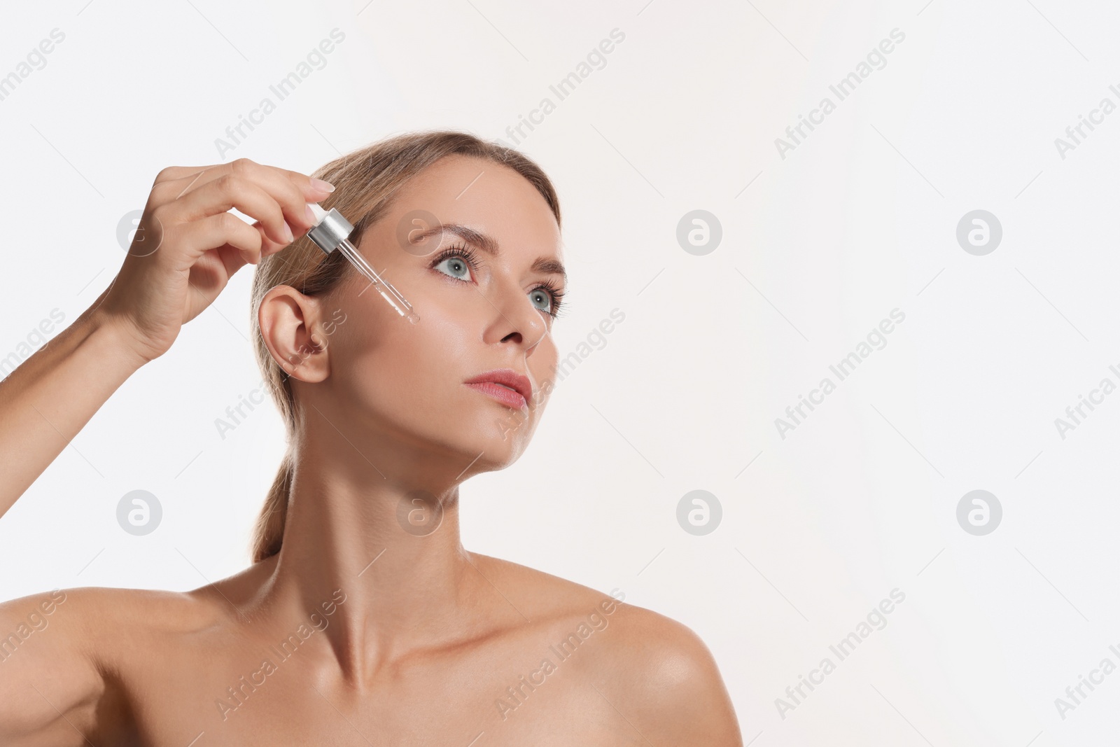 Photo of Beautiful woman applying cosmetic serum onto her face on white background, space for text