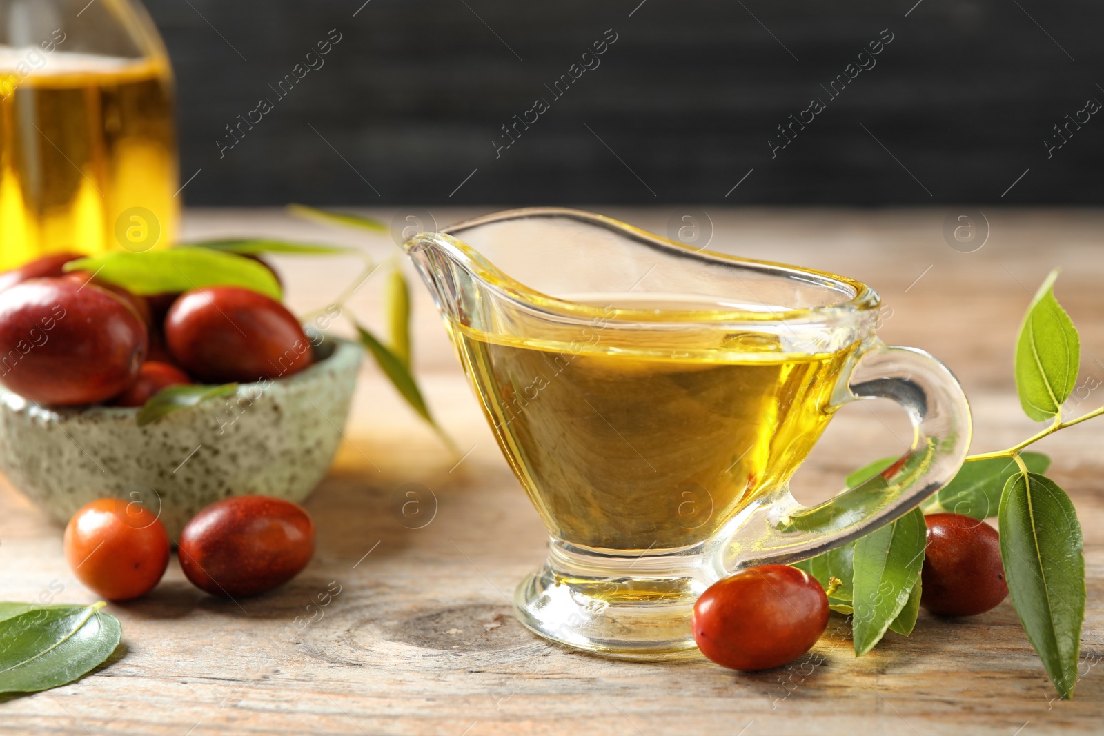 Photo of Glass sauce boat with jojoba oil and seeds on wooden table