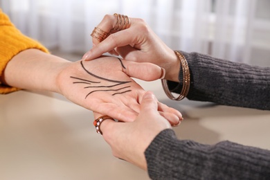 Chiromancer reading lines on woman's palm at table, closeup