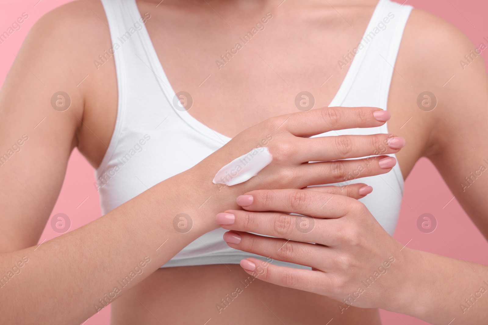 Photo of Woman with smear of body cream on her hand against pink background, closeup