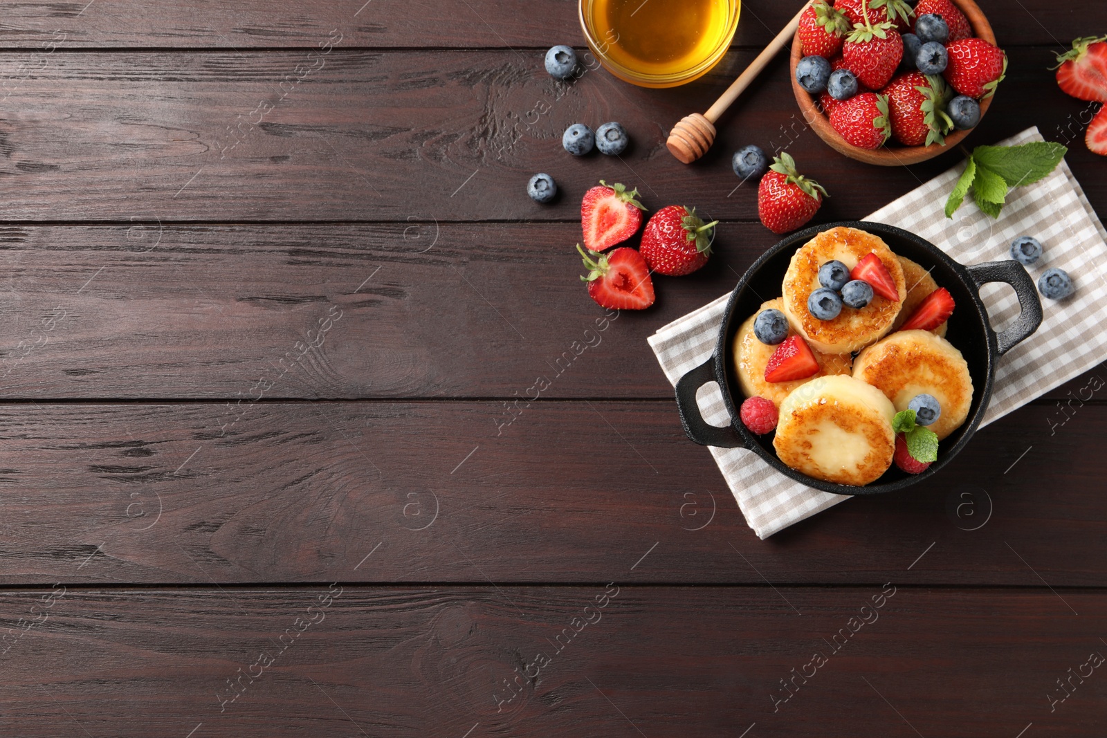 Photo of Delicious cottage cheese pancakes with fresh berries and honey on wooden table, flat lay. Space for text