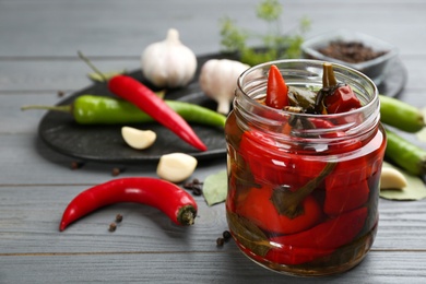 Photo of Glass jar of pickled chili peppers on grey wooden table. Space for text