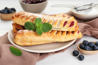 Photo of Fresh tasty puff pastry with sugar powder, mint and blueberries on white wooden table, closeup