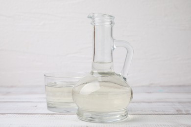 Photo of Vinegar in glass jug and bowl on white wooden table