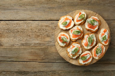 Photo of Tasty canapes with salmon, cucumber, cream cheese and dill on wooden stand, top view. Space for text