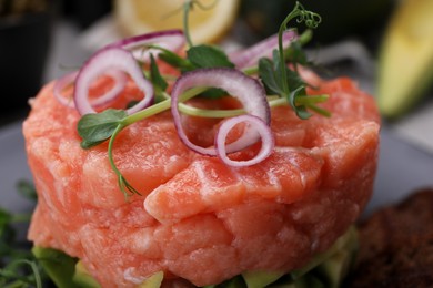 Tasty salmon tartare with microgreens and red onion on plate, closeup