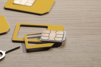 Photo of Different SIM cards and ejector on wooden background, closeup