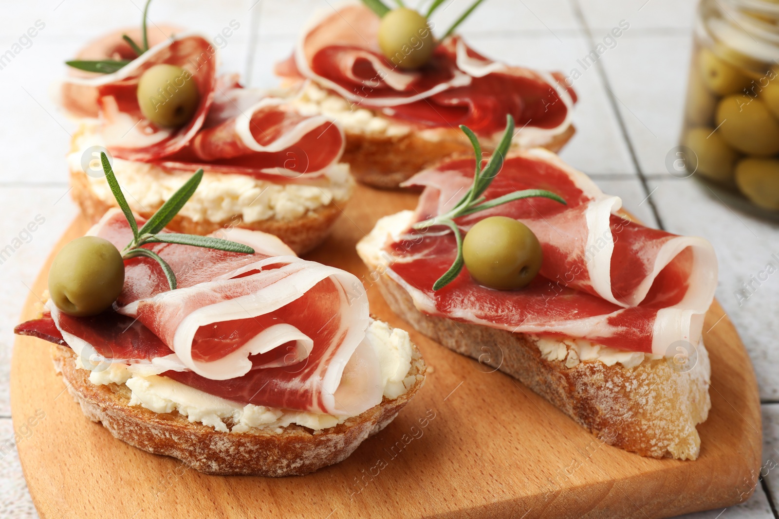 Photo of Tasty sandwiches with cured ham, rosemary and olives on wooden board, closeup
