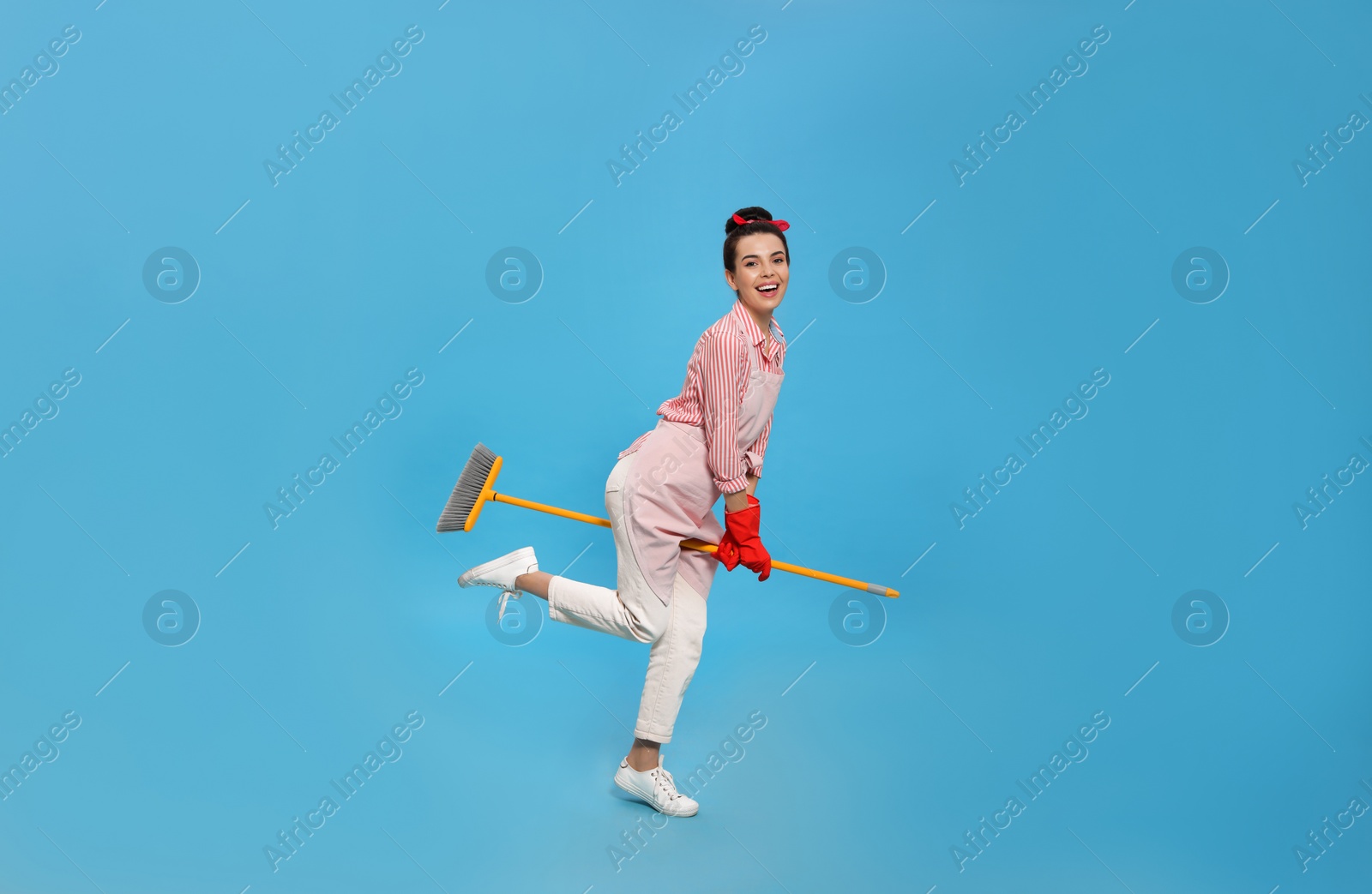 Photo of Young housewife with broom having fun on light blue background