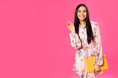 Young woman wearing floral print dress with elegant clutch on pink background. Space for text