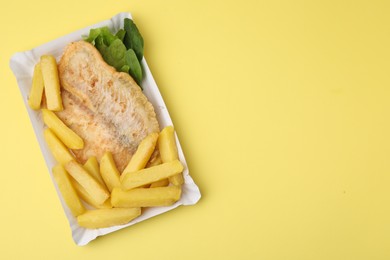 Photo of Delicious fish and chips with spinach and lettuce on yellow table, top view. Space for text