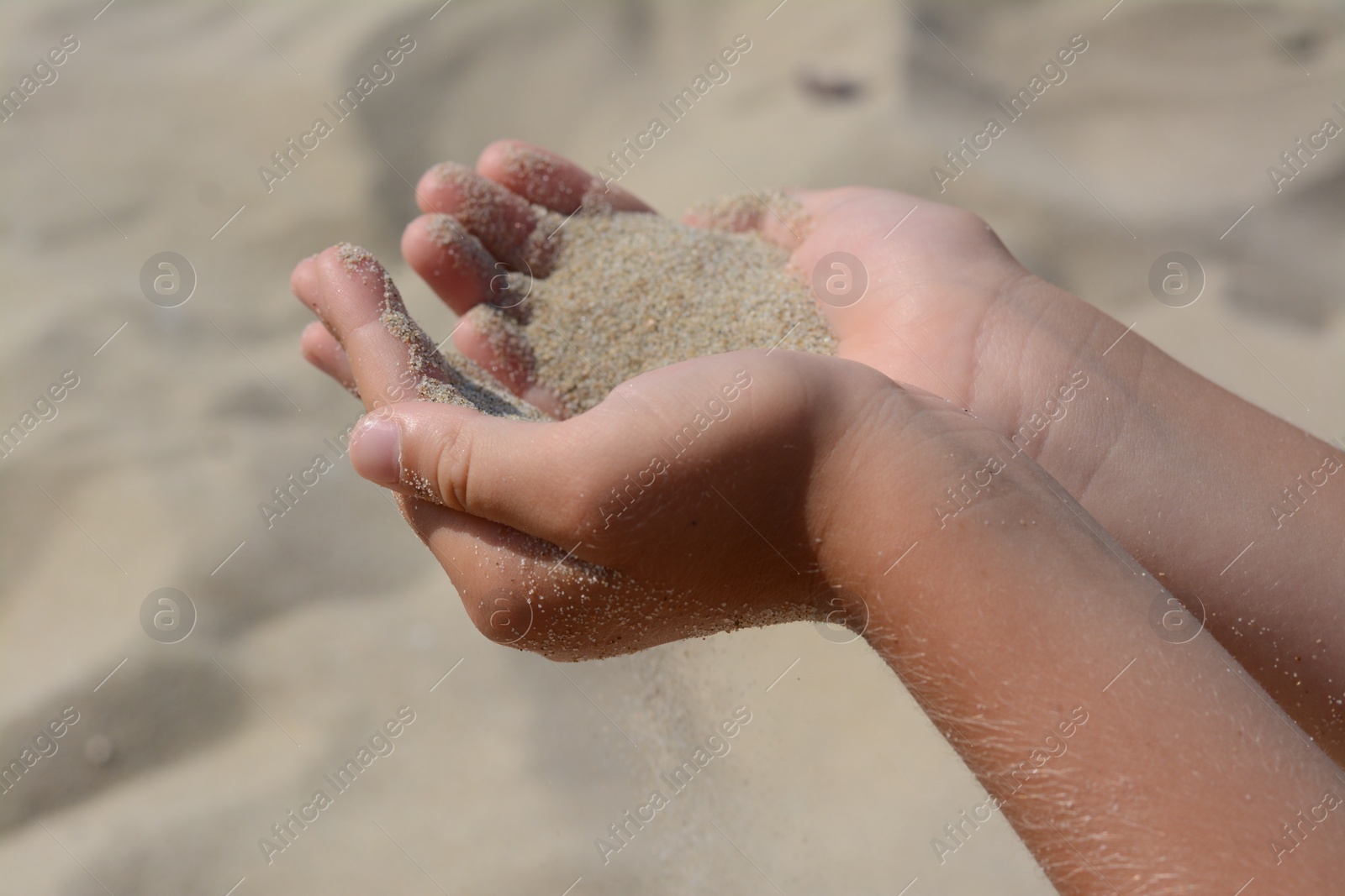 Photo of Child pouring sand from hands outdoors, closeup. Fleeting time concept