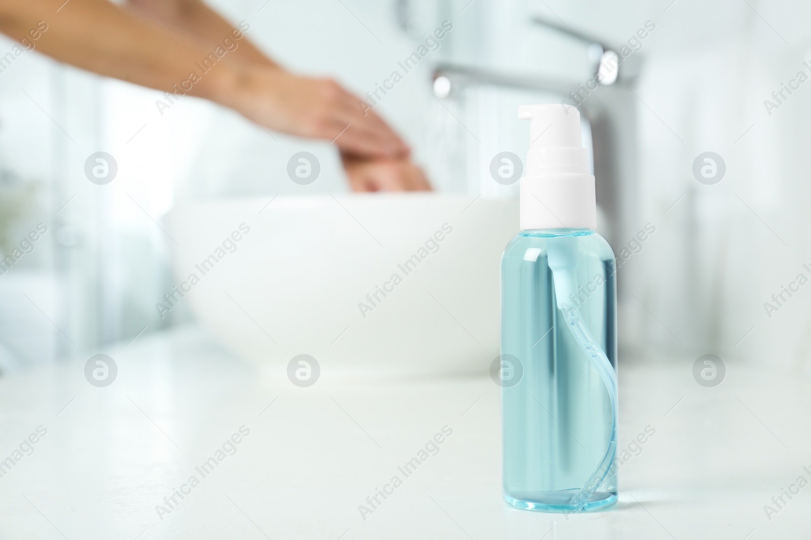 Photo of Bottle of antibacterial soap and blurred woman washing hands on background. Personal hygiene during COVID-19 pandemic