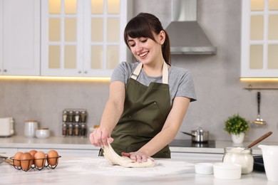 Happy young housewife kneading dough at white marble table in kitchen