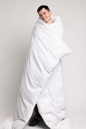 Happy man in pyjama wrapped in blanket on light grey background