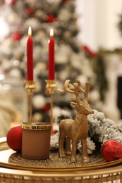 Photo of Christmas composition with decorative reindeer and candles on golden table in room, closeup