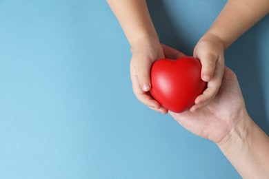 Mother and her child holding red decorative heart on light blue background, top view. Space for text