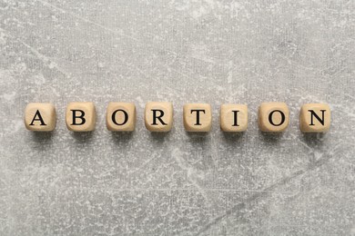 Photo of Word Abortion made of wooden cubes on grey background, flat lay