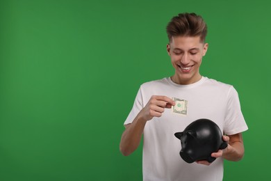 Photo of Happy man putting dollar banknote into piggy bank on green background. Space for text