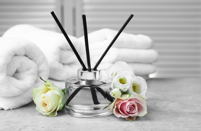 Photo of Towels, reed air freshener and flowers on grey table indoors