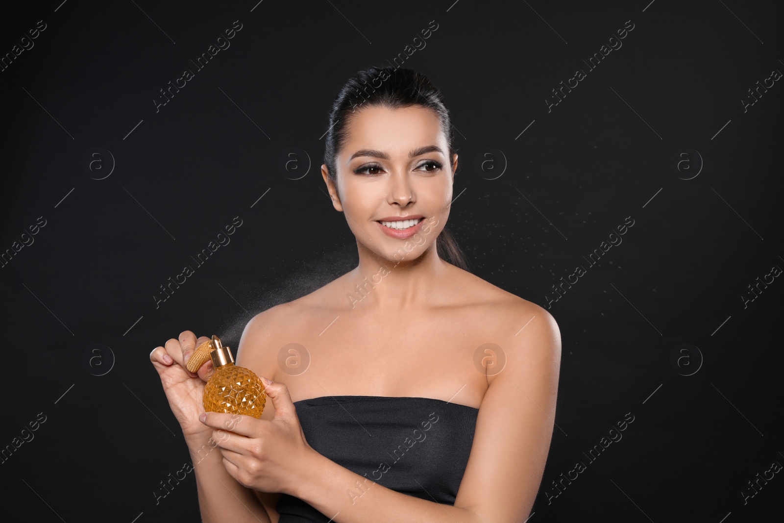 Photo of Young woman spraying perfume on black background