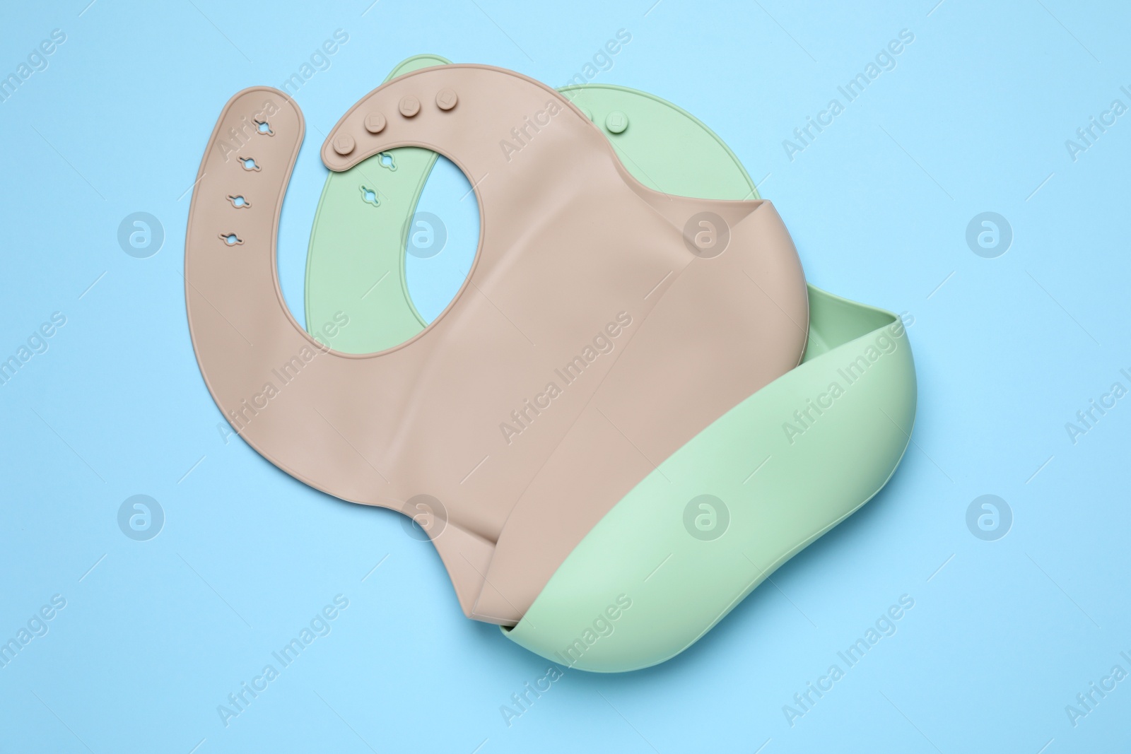 Photo of Two silicone baby bibs on light blue background, top view. First food