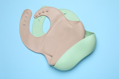 Photo of Two silicone baby bibs on light blue background, top view. First food