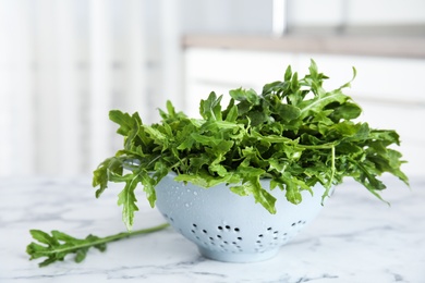 Fresh arugula in colander on white marble table indoors