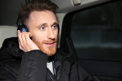 Young man listening to music with headphones in car. Space for text