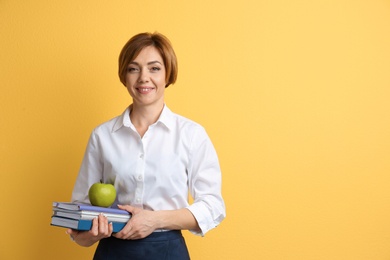 Portrait of female teacher with notebooks and apple on color background