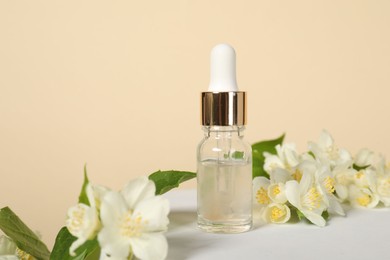 Presentation of essential oil in bottle and beautiful jasmine flowers against beige background, closeup