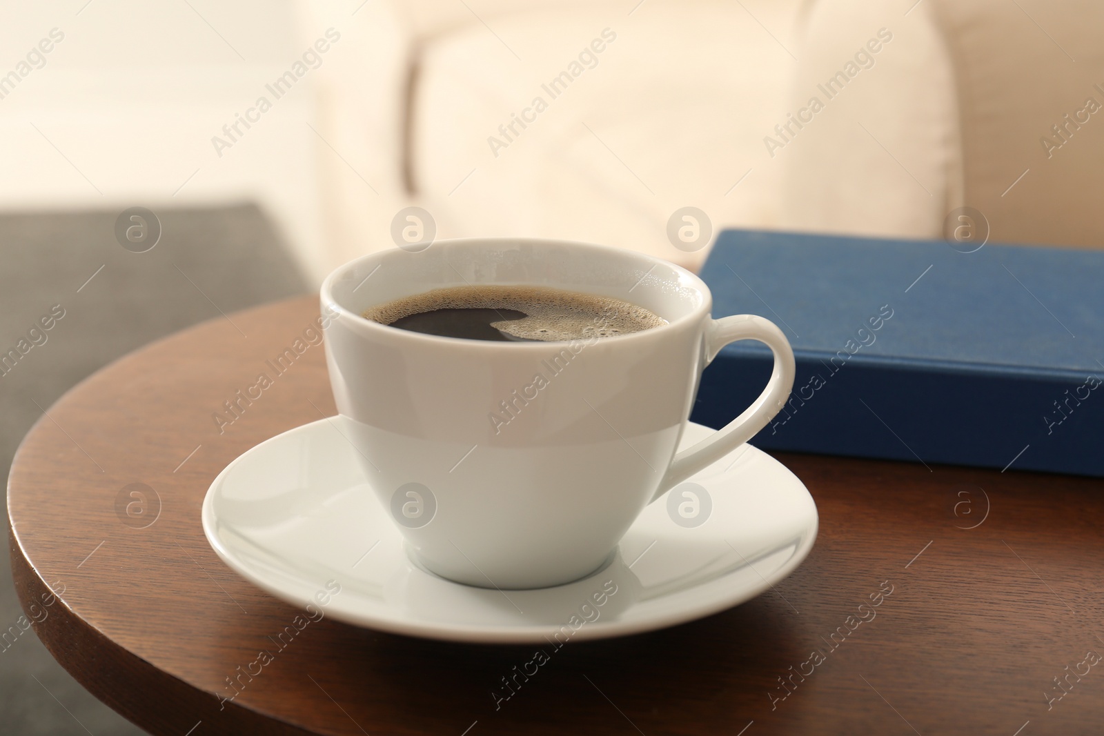 Photo of Cup of coffee and book on table in room