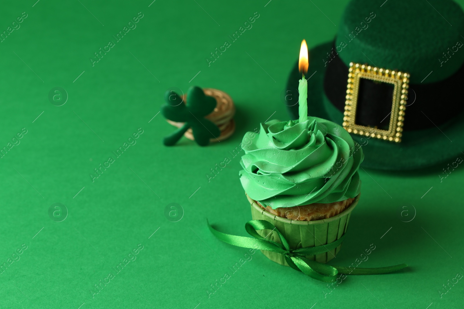 Photo of St. Patrick's day party. Tasty cupcake with burning candle and leprechaun hat on green background. Space for text