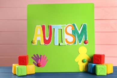 Magnetic board with word Autism, paper human figure and colorful cubes on blue wooden table