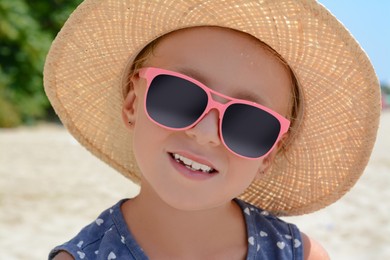 Photo of Little girl wearing sunglasses and hat at beach on sunny day