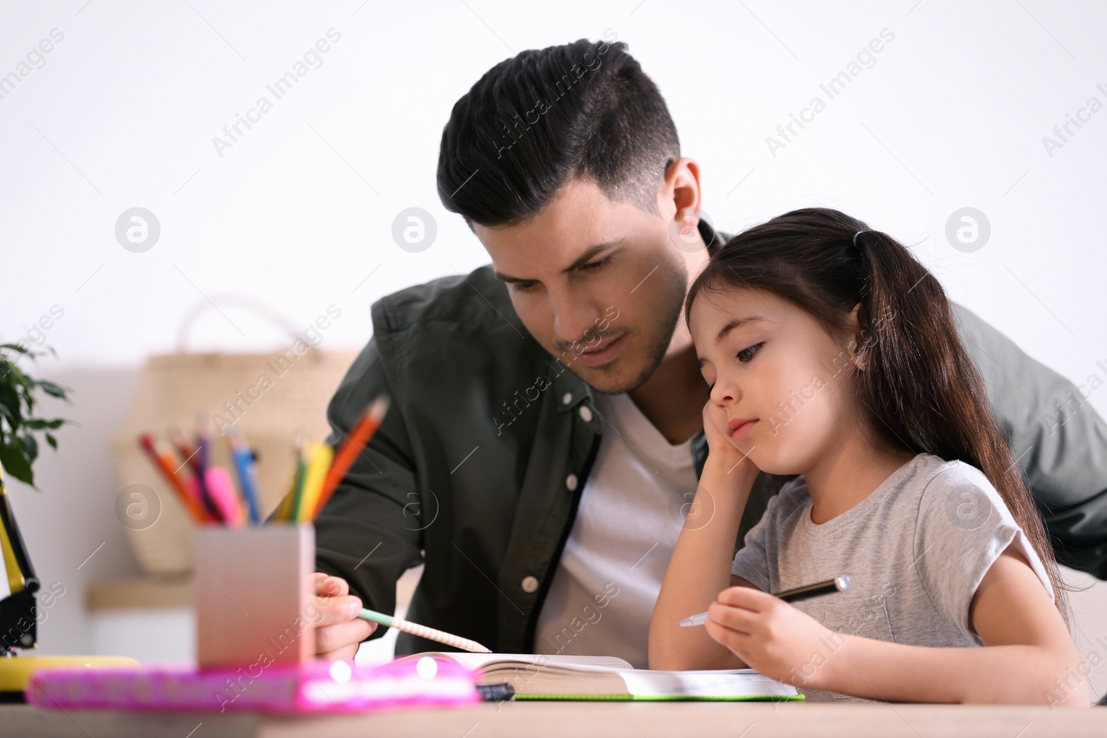 Photo of Man helping his daughter with homework at table indoors