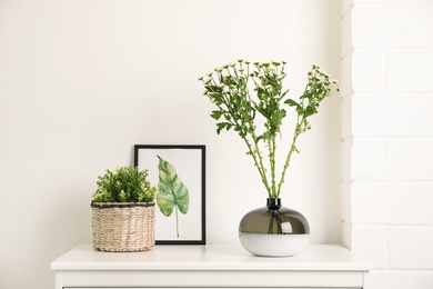 Photo of Decorative vase with flowers and houseplant on commode indoors