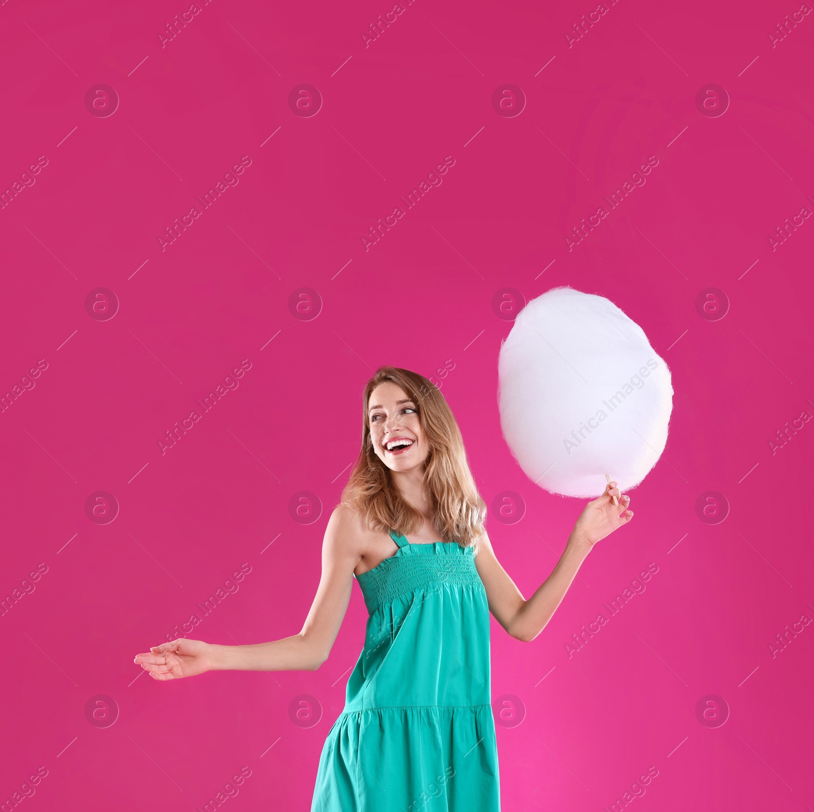 Photo of Happy young woman with cotton candy on pink background