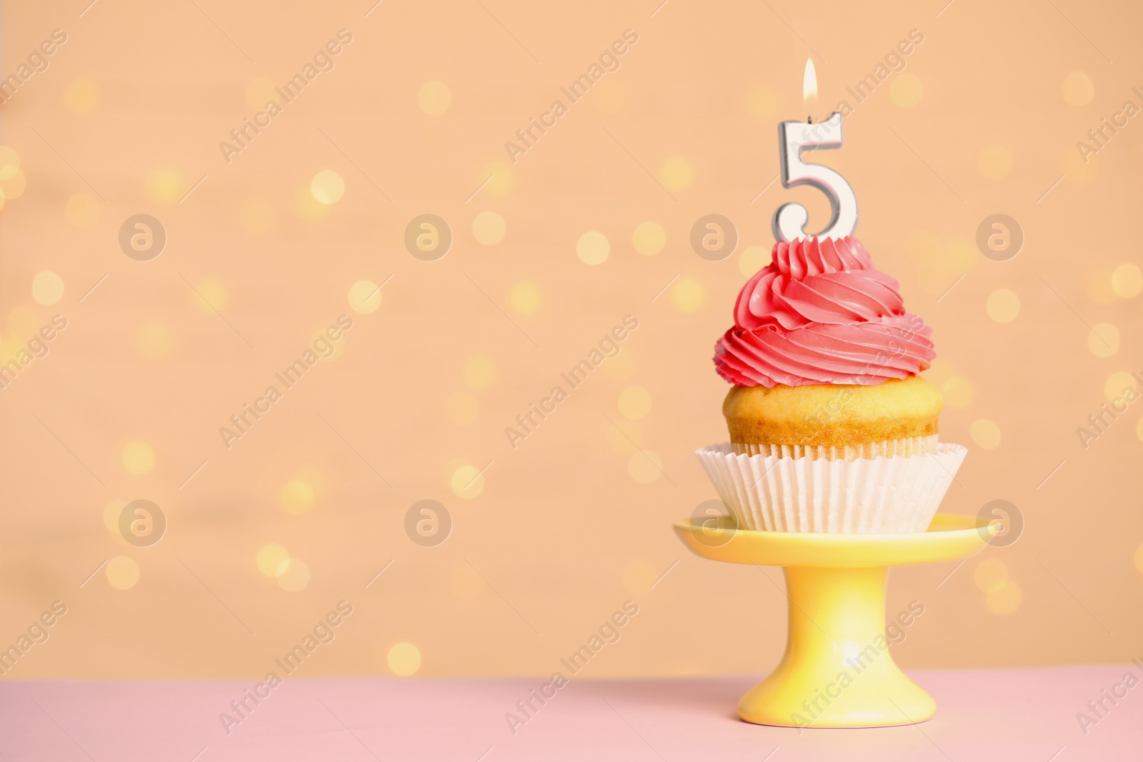 Photo of Birthday cupcake with number five candle on stand against festive lights, space for text