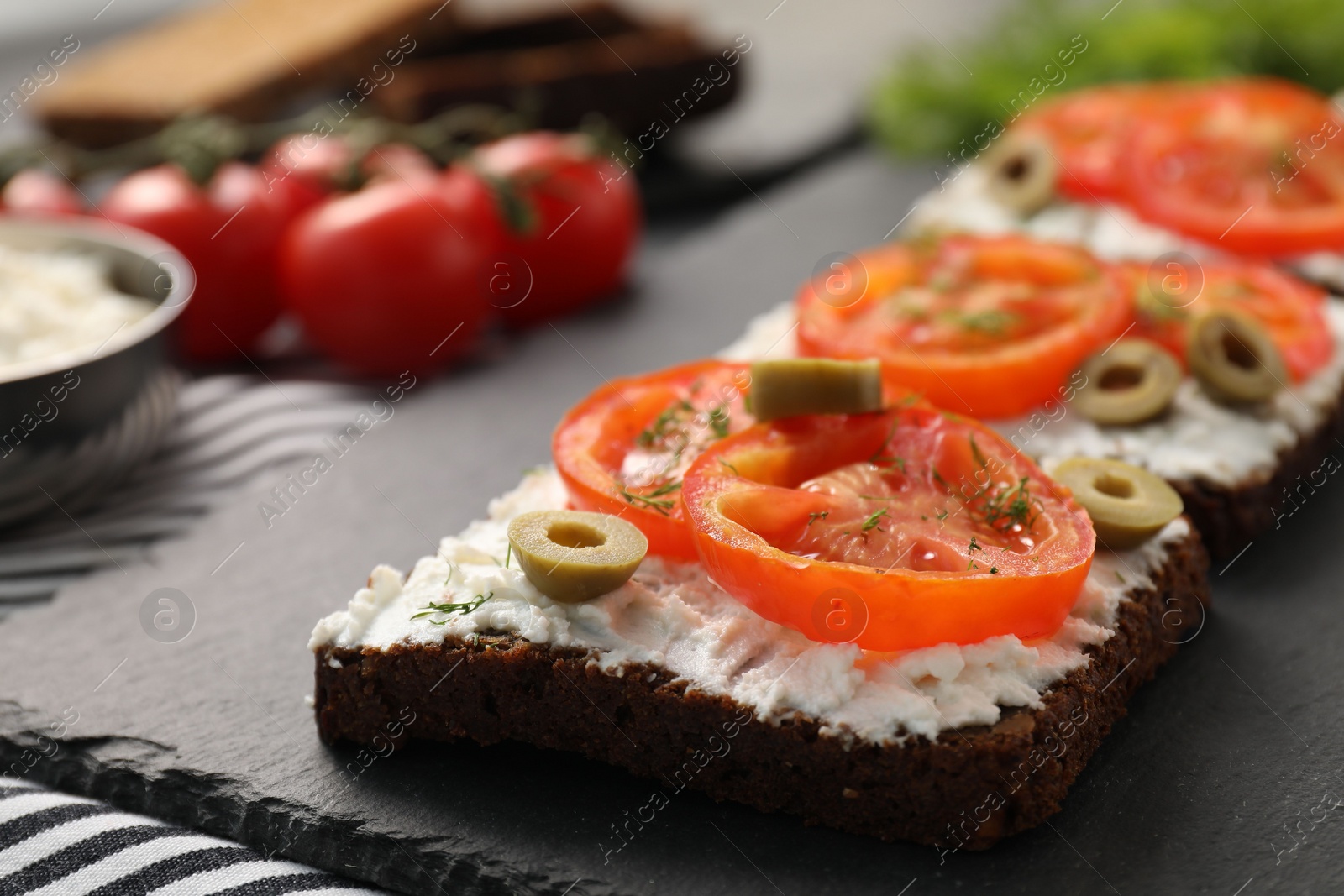 Photo of Delicious ricotta bruschettas with sliced tomatoes, olives and greens on black table, closeup