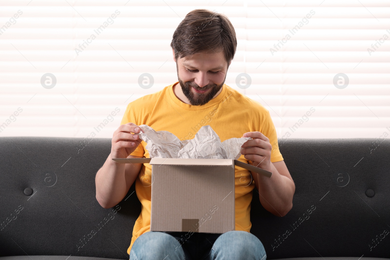 Photo of Happy man opening parcel at home. Internet shopping