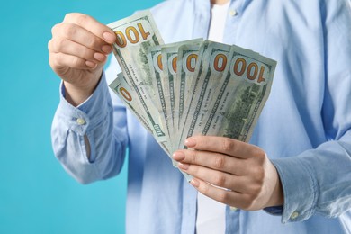 Photo of Woman counting dollar banknotes on turquoise background, closeup. Money exchange concept