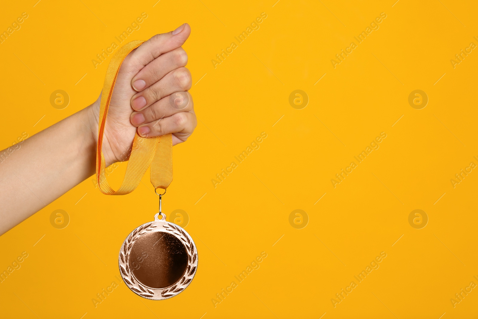 Photo of Woman holding silver medal on yellow background, closeup. Space for design