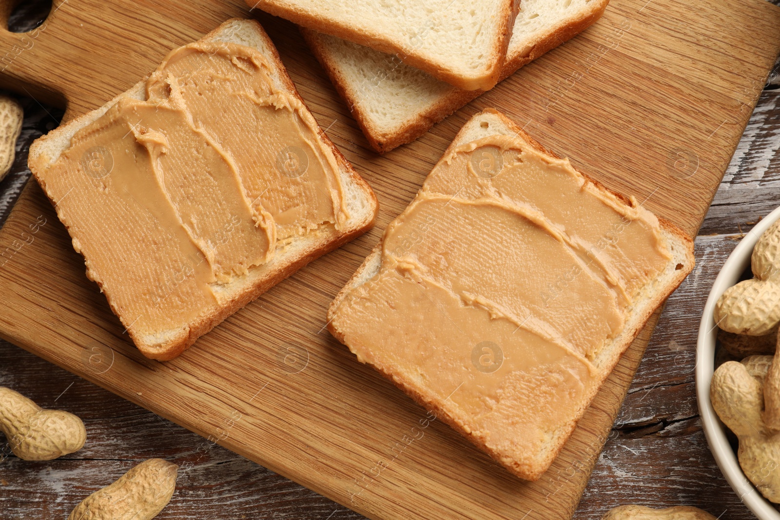 Photo of Tasty peanut butter sandwiches and peanuts on wooden table, flat lay