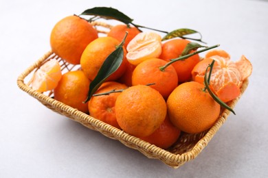 Photo of Fresh ripe tangerines with green leaves in wicker basket on white table