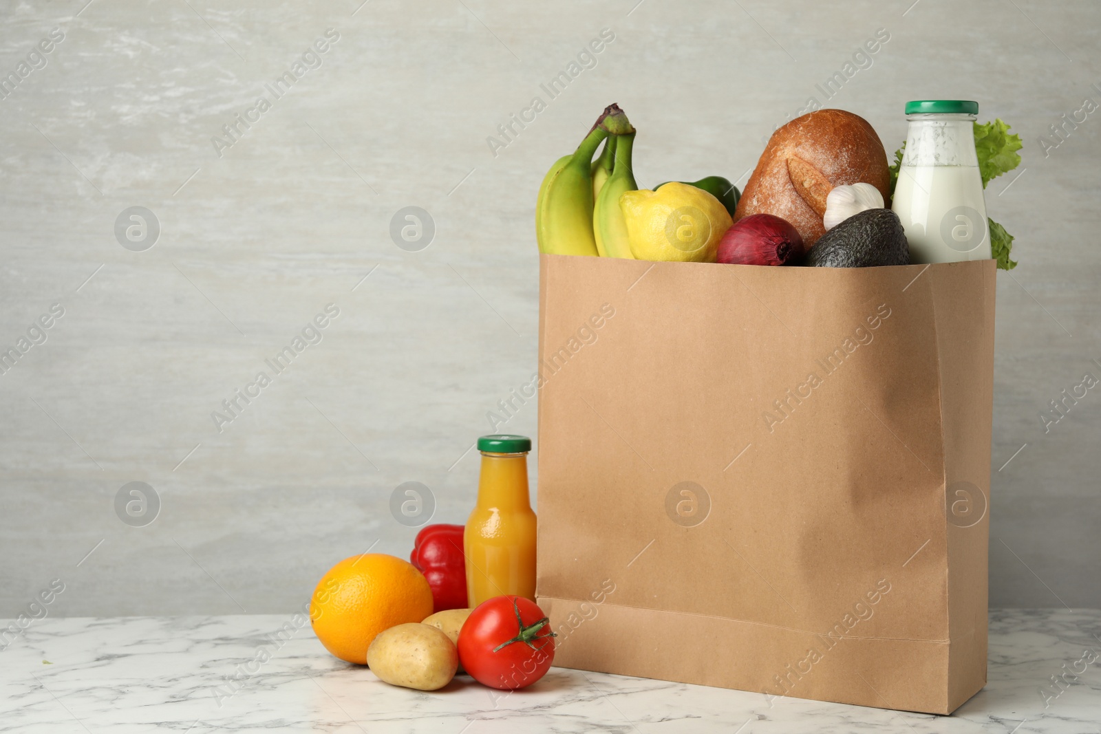 Photo of Paper bag with groceries on marble table against grey background. Space for text