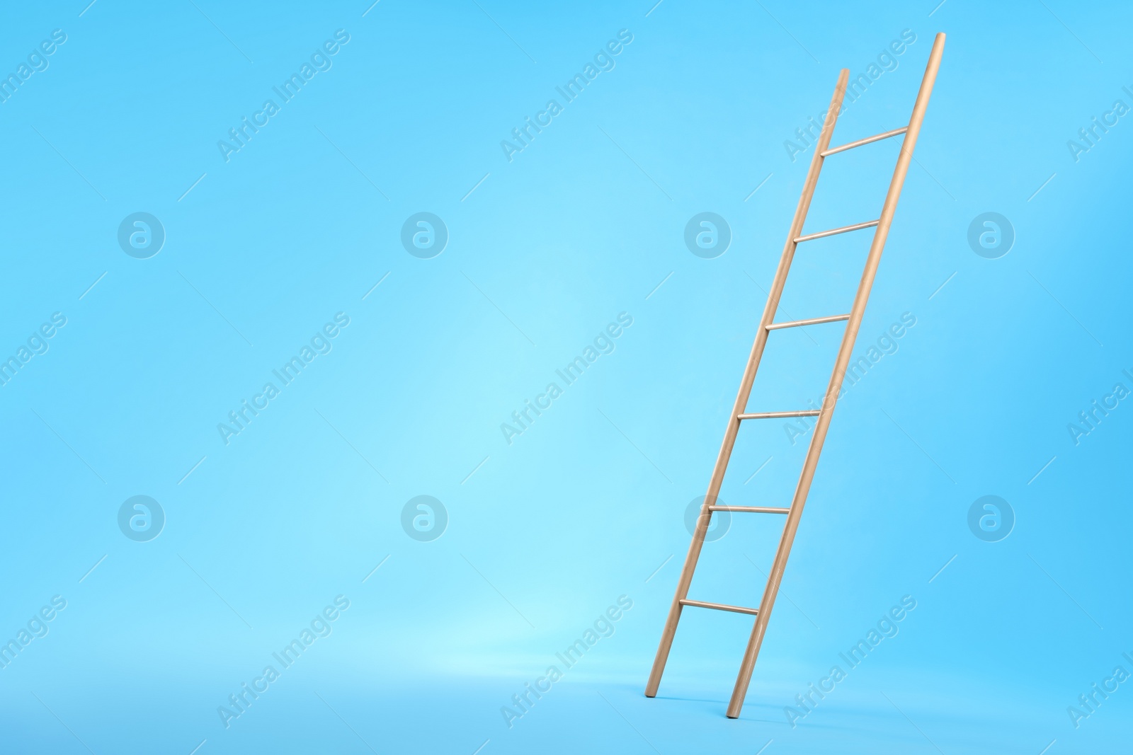 Photo of Modern wooden ladder on light blue background. Space for text