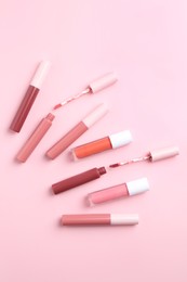 Photo of Different lip glosses and applicators on pink background, flat lay