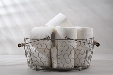 Photo of Soft toilet paper rolls in metal basket on white wooden table, closeup